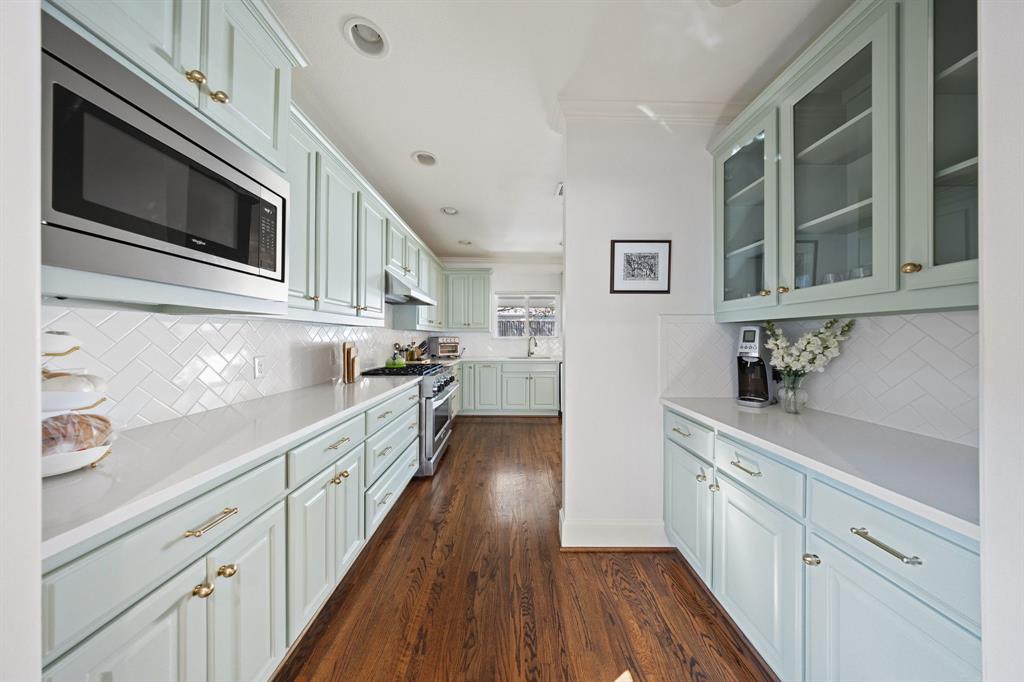 Recessed lighting illuminates the galley-style kitchen featuring light-toned cabinetry, white herringbone tile backsplash, integrated stainless steel microwave, and wood-finish flooring