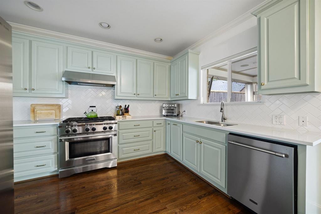 Light-hued cabinetry with ample storage, stainless steel appliances, wood-finish flooring, white countertops, and a herringbone pattern tile backsplash
