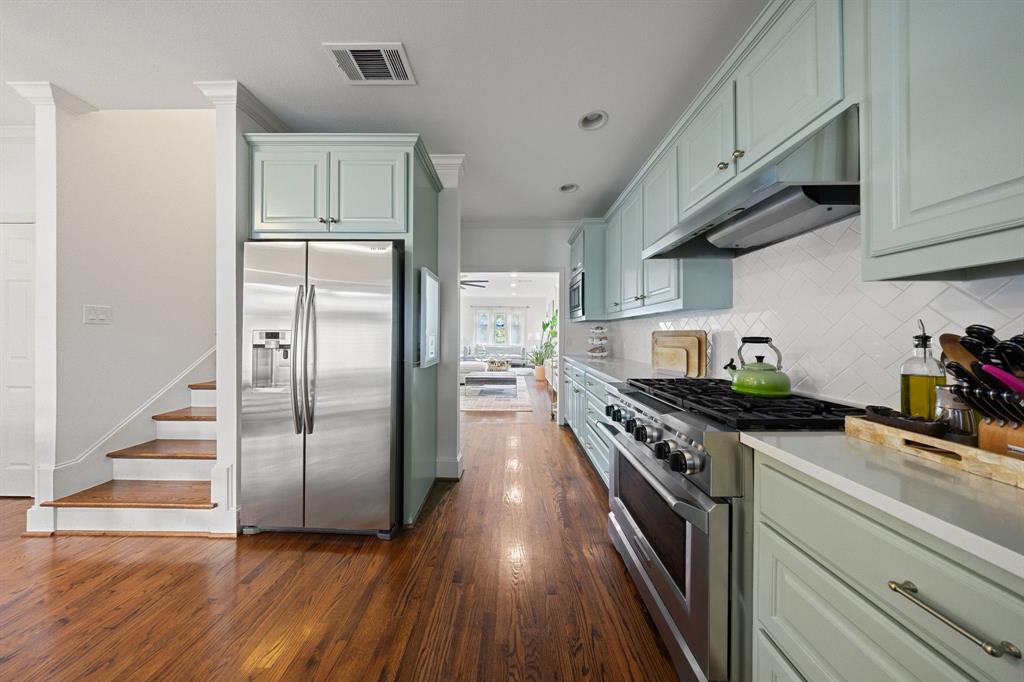 Hardwood flooring throughout, stainless steel refrigerator, stainless steel range, light-toned cabinetry, and white tile backsplash