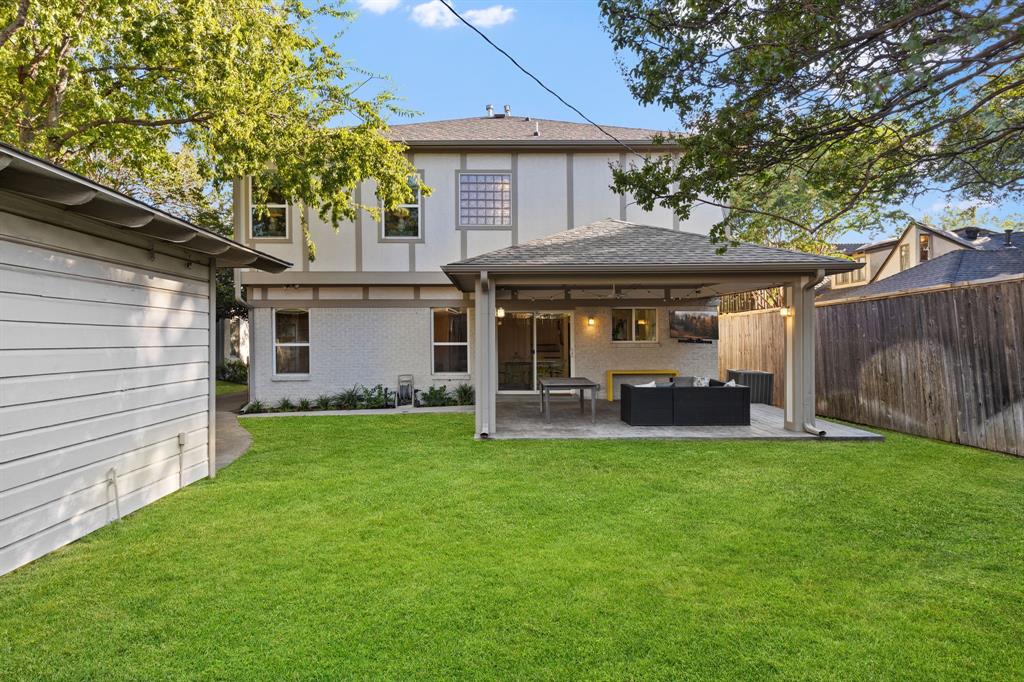 Expansive green lawn, covered patio area, stucco exterior, privacy fencing, and a detached structure
