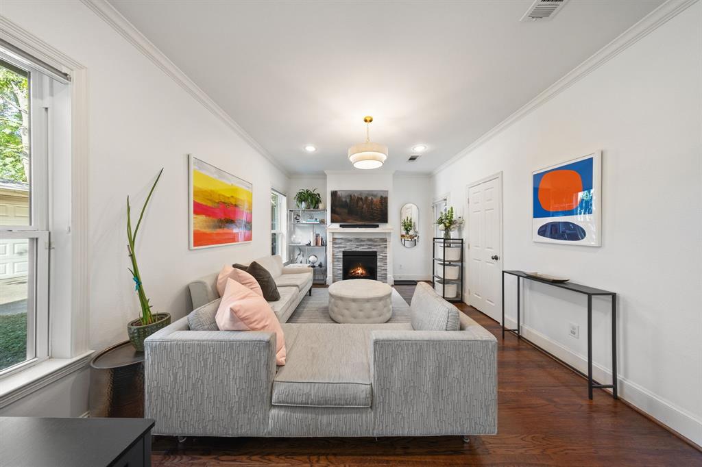 Hardwood flooring, recessed lighting, crown molding, white walls, and a stone-clad fireplace