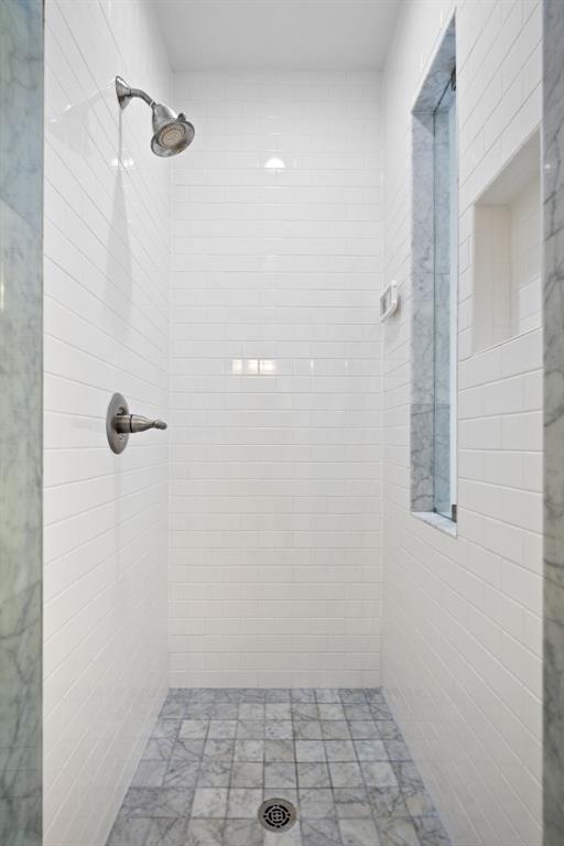 White subway tile shower surround with a built-in niche and window, featuring a brushed nickel shower head and controls, and a grey tile floor with a central drain