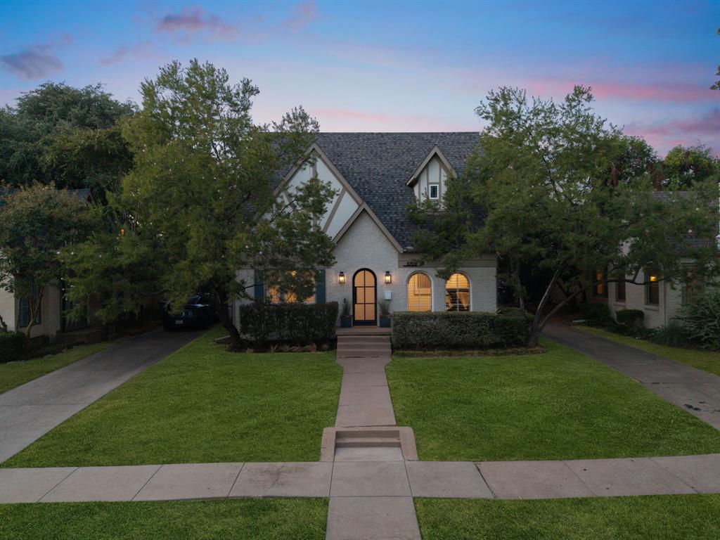Tudor-style exterior with a dark shingle roof, arched entry door, light brick facade, and dormer windows