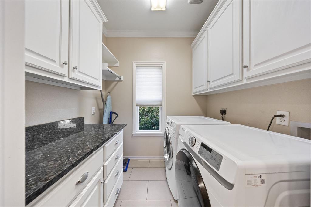 White cabinetry with brushed nickel hardware, dark speckled countertop, single window with blinds, overhead lighting, and tile flooring
