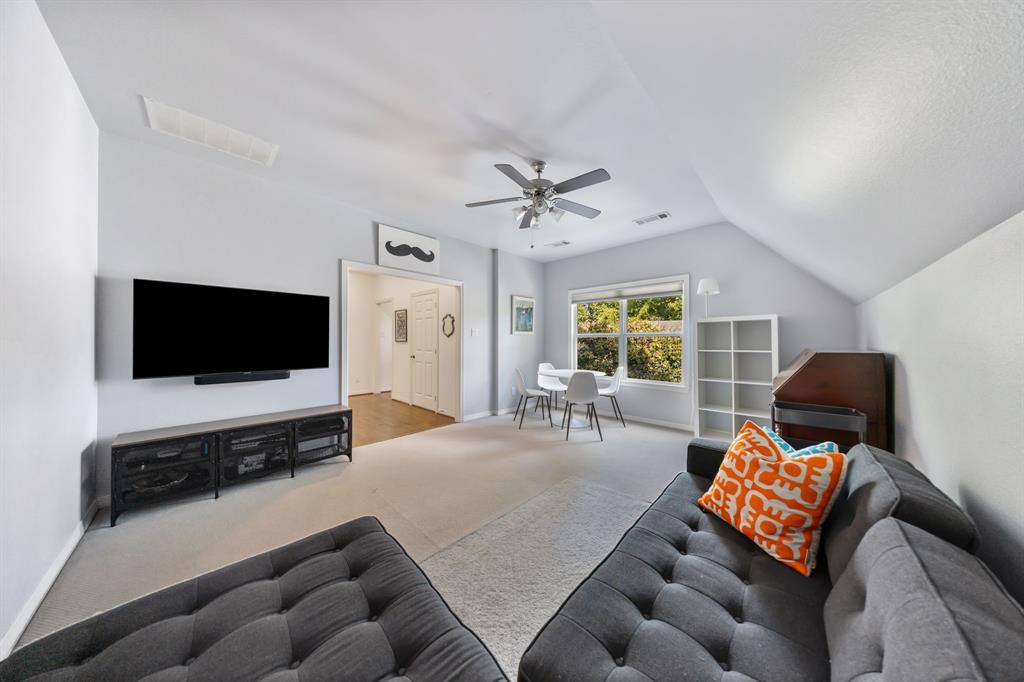 Spacious carpeted room featuring a ceiling fan, vaulted ceilings, and a window with exterior views