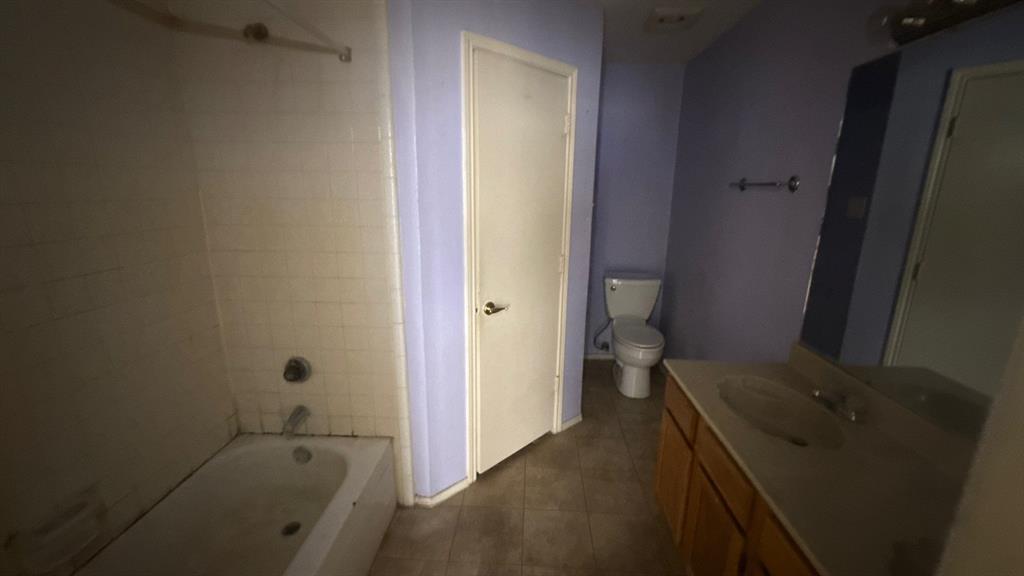 Bathroom featuring a built-in tub with tile surround, a single vanity with an integrated sink, a large wall-mounted mirror, and tile flooring