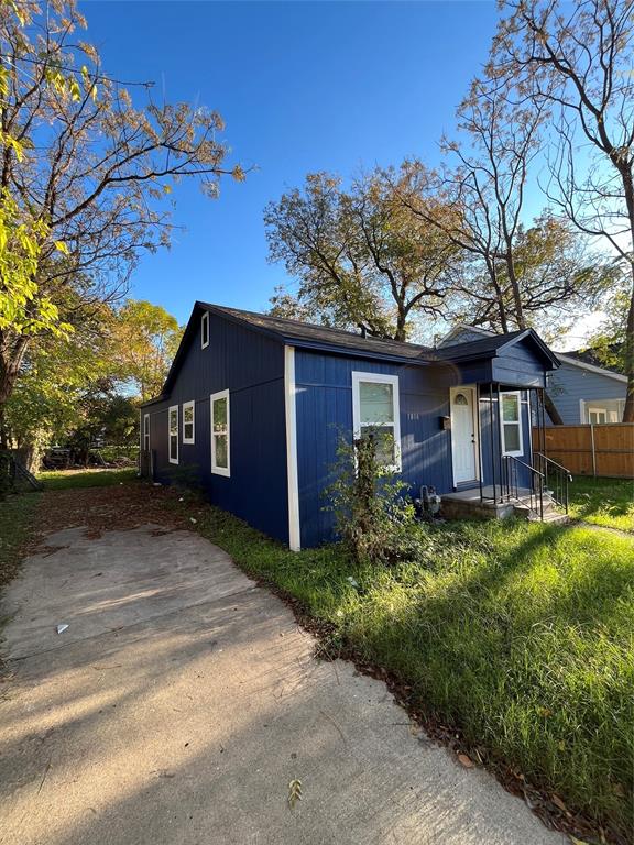 Exterior featuring blue vertical siding, a front porch with metal railing, concrete driveway, and mature trees