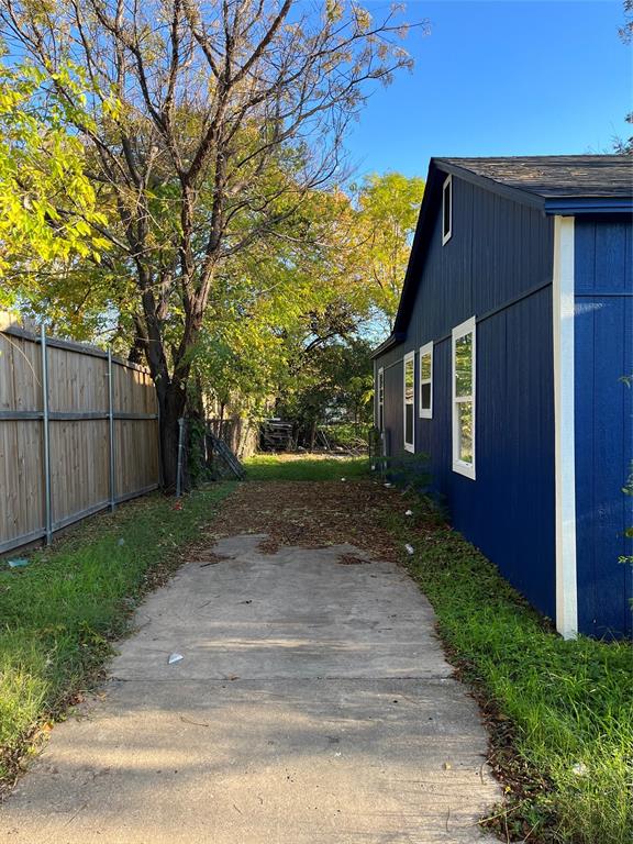 Exterior side yard featuring a concrete path, wood-panel siding, and a wooden privacy fence