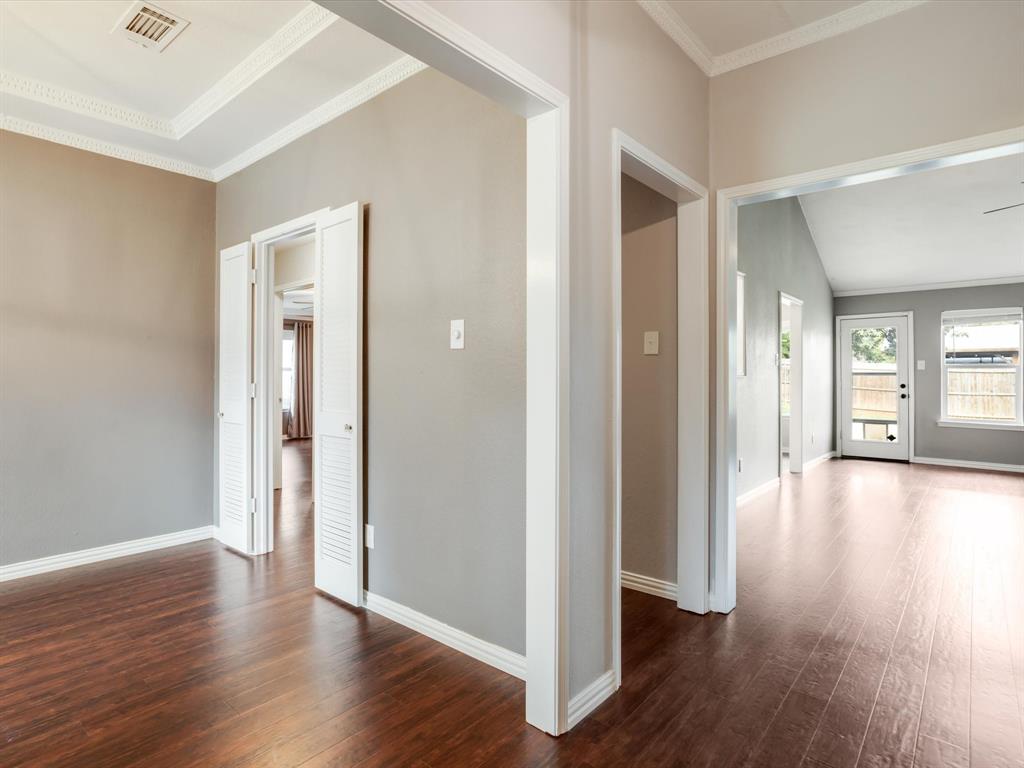 Interior featuring wood-finish flooring, crisp crown molding, recessed tray ceiling detailing, and white louvered closet doors