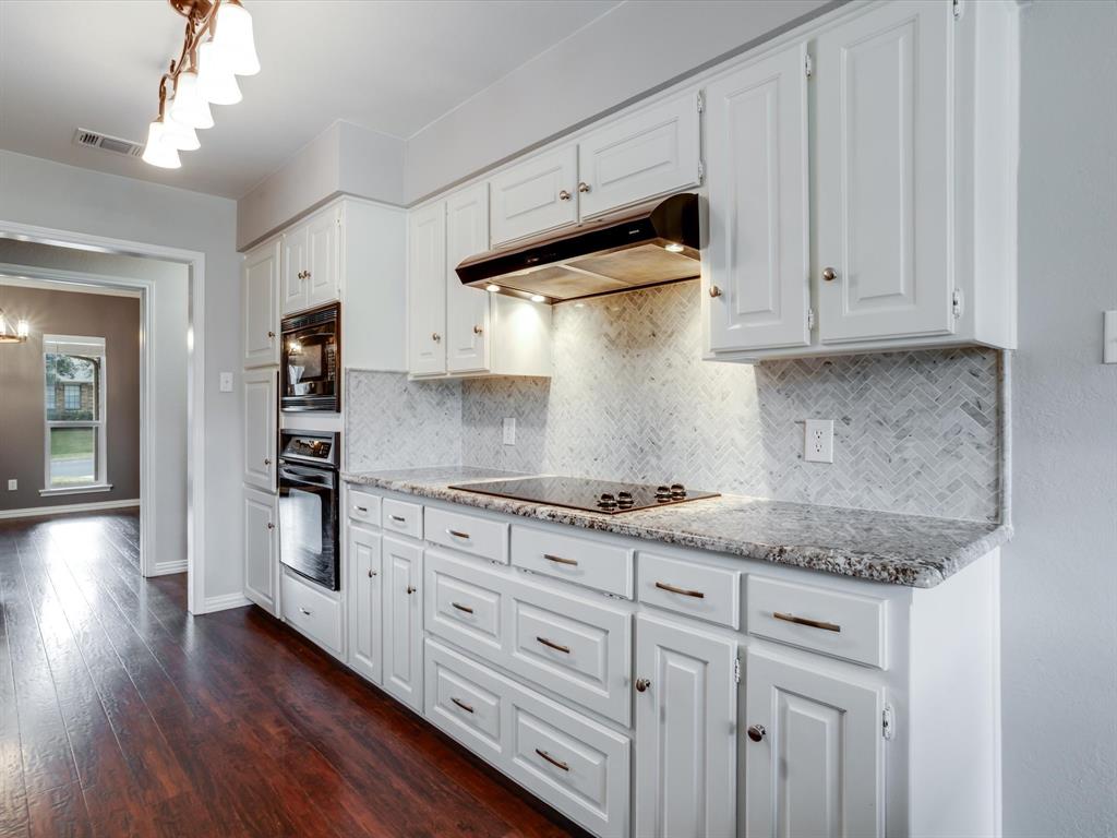 Kitchen featuring white cabinetry, stone-surface countertops, herringbone-pattern tile backsplash, built-in wall oven and microwave, and wood-finish flooring