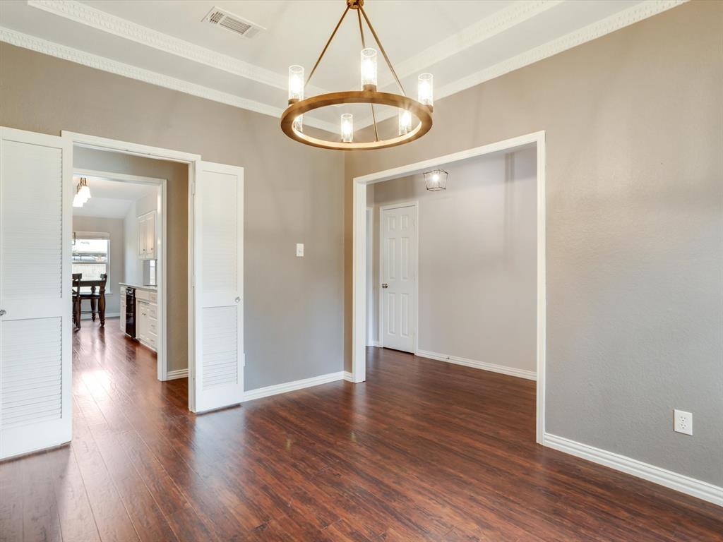 Circular chandelier with metallic finish and glass shades, tray ceiling with crown molding, and wood-finish flooring