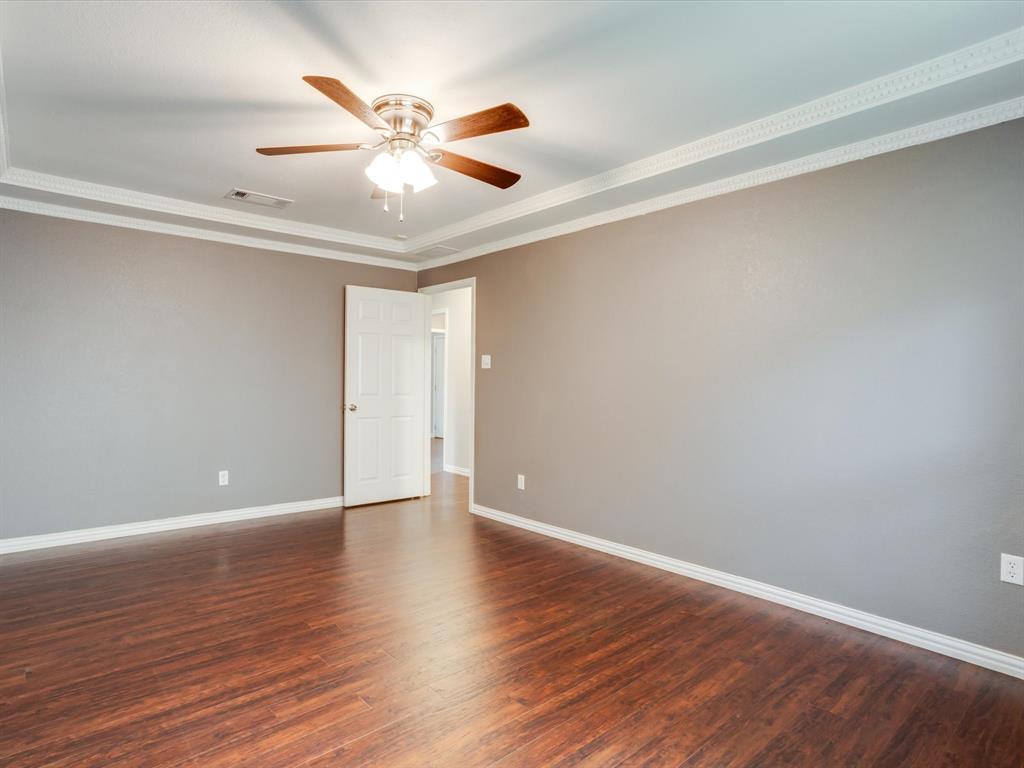 Room featuring wood-finish flooring, a tray ceiling with decorative crown molding, and a central ceiling fan with integrated lighting