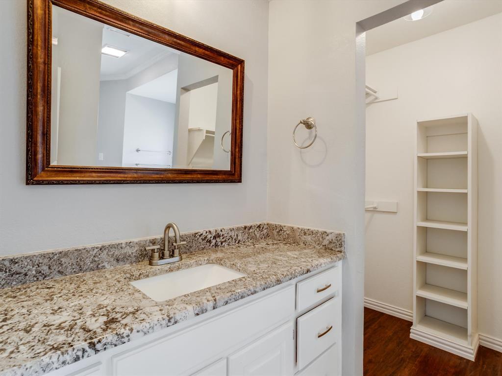 Stone countertop vanity with undermount sink, white cabinetry with silver-tone hardware, framed mirror, brushed nickel faucet, and built-in shelving unit