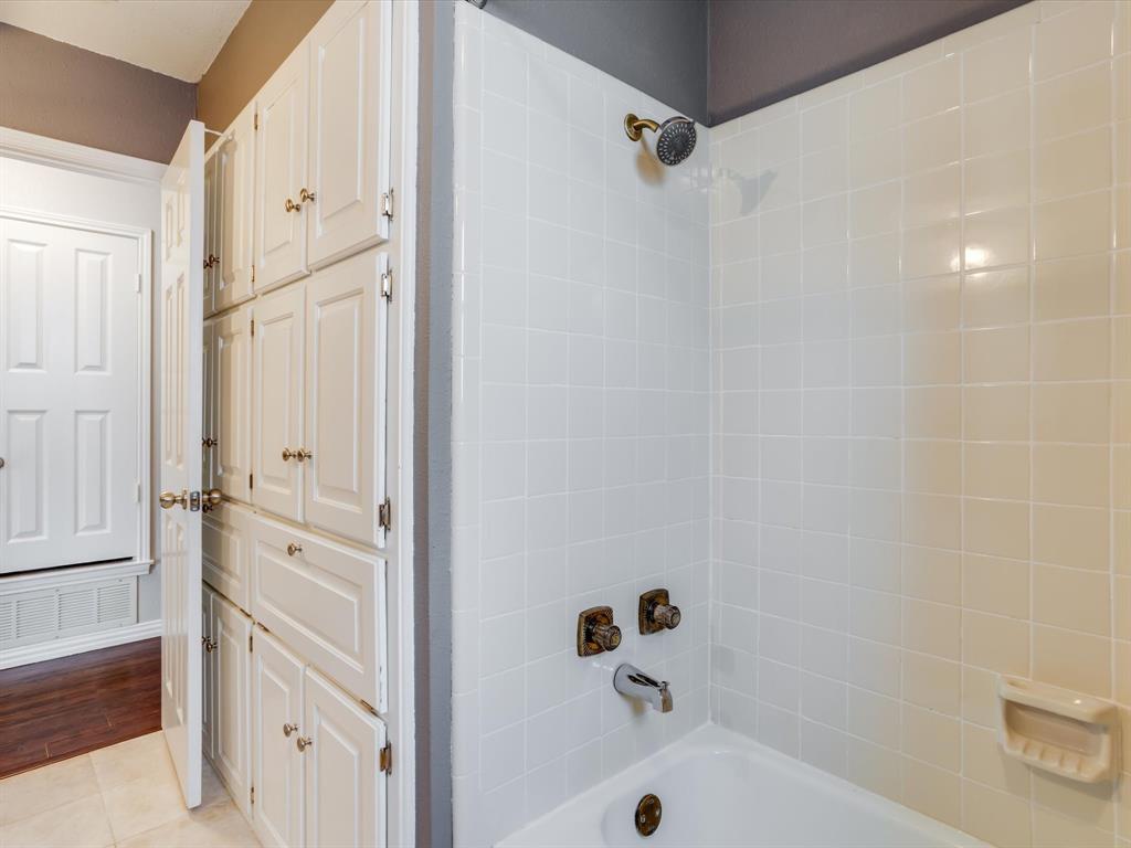 Full-height built-in cabinetry, shower-tub combination with white tile surround, and metallic-finish hardware