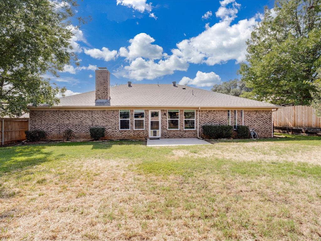 Rear exterior featuring a full brick facade, masonry chimney, concrete patio, and fenced backyard
