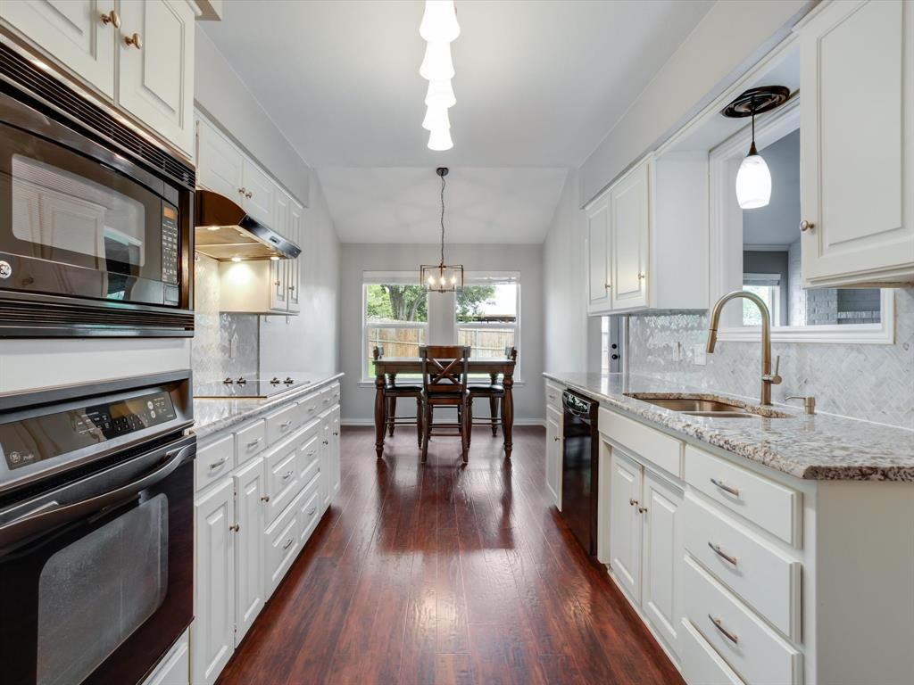 Kitchen featuring white shaker-style cabinetry, stone-finish countertops, wood-finish flooring, a herringbone-pattern tile backsplash, and built-in stainless steel appliances