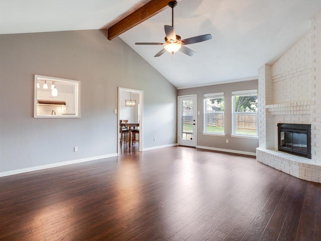 Vaulted ceiling featuring an exposed wood beam, wood-finish flooring, painted brick fireplace, and an integrated ceiling fan with lighting