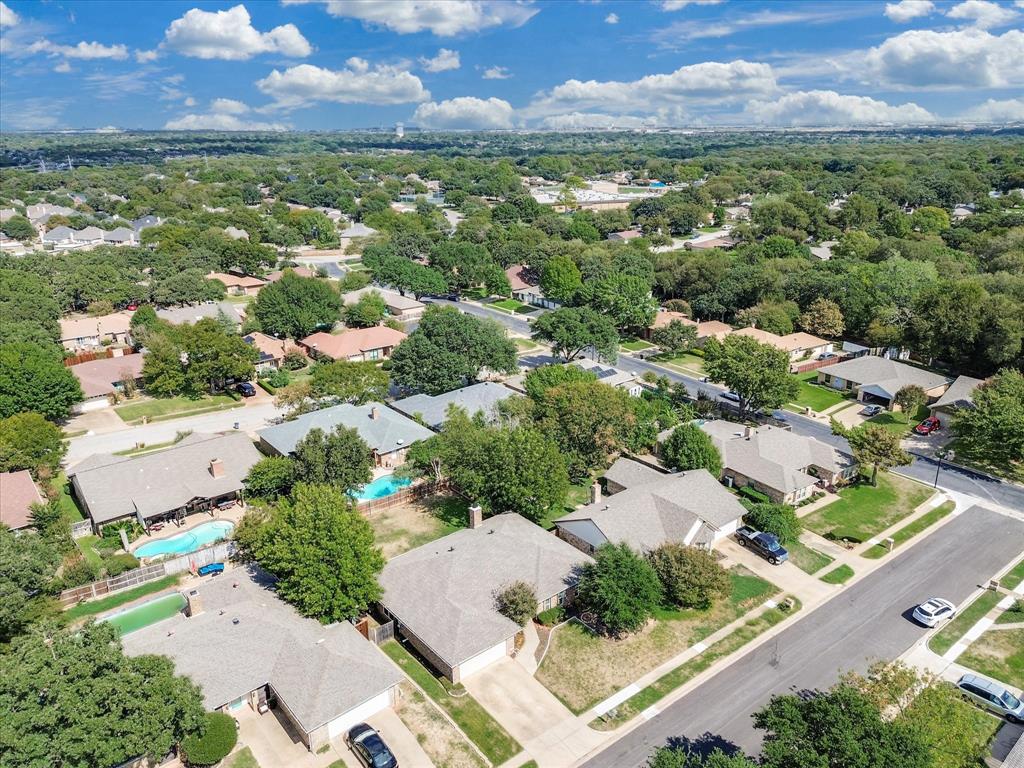 Aerial perspective of a residential neighborhood featuring mature trees, paved streets, and properties with integrated swimming pools