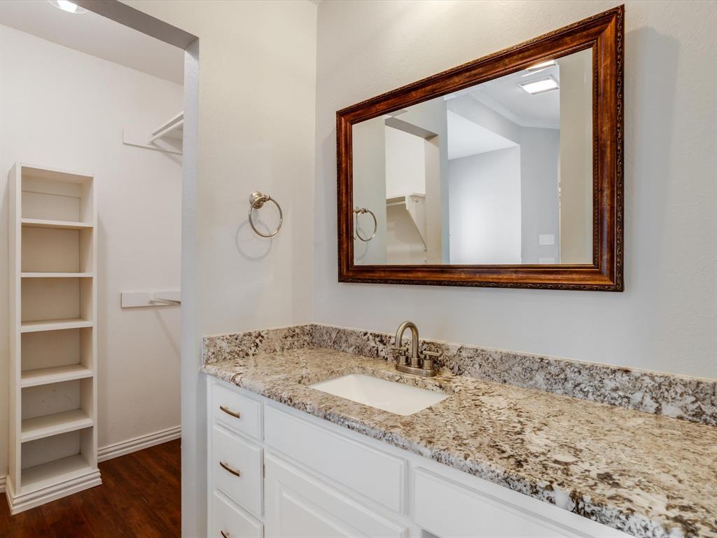 Vanity featuring a stone-look countertop, white shaker-style cabinetry, an integrated rectangular sink with a brushed metal faucet, a framed mirror, and built-in shelving
