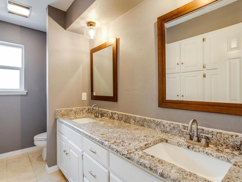 Dual-sink vanity with stone-finish countertop, white cabinetry, integrated rectangular basins, and framed wall mirrors