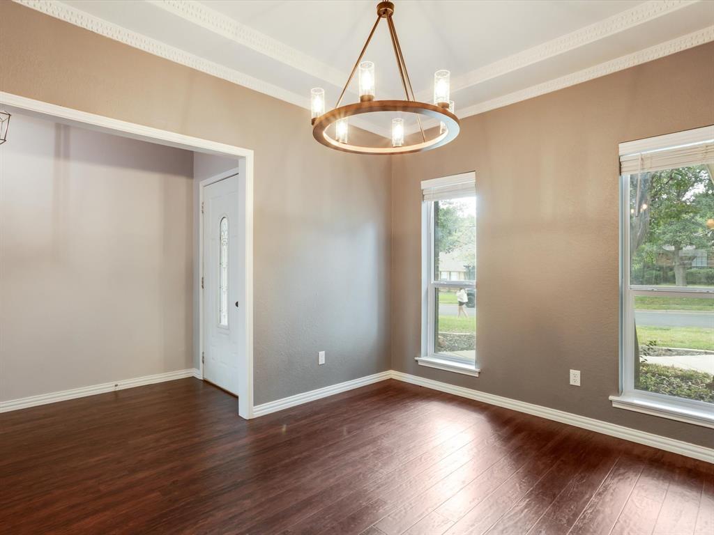Wood-finish flooring, crown molding, circular bronze-tone chandelier with cylindrical glass shades, and two tall windows with light-filtering blinds