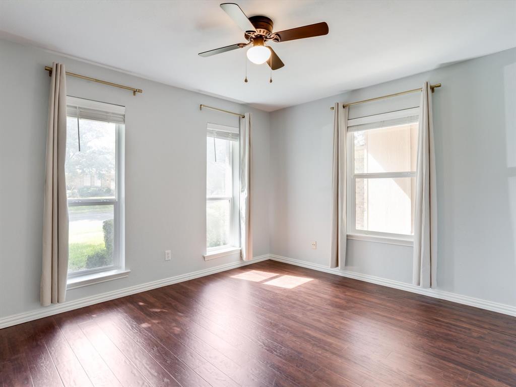 Room featuring wood-finish flooring, three double-pane windows, and a central ceiling fan with an integrated light fixture