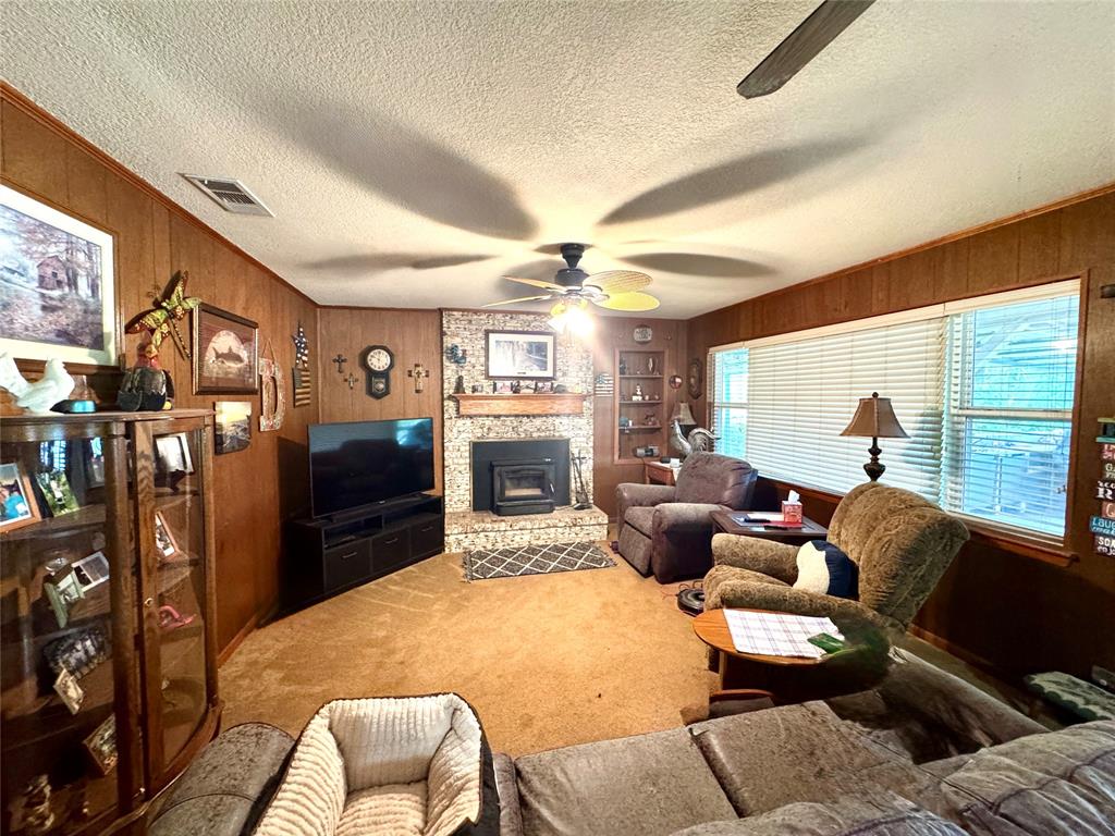 Brick-faced fireplace with a hearth insert, wood paneling, built-in shelving, ceiling fan, and carpeted flooring