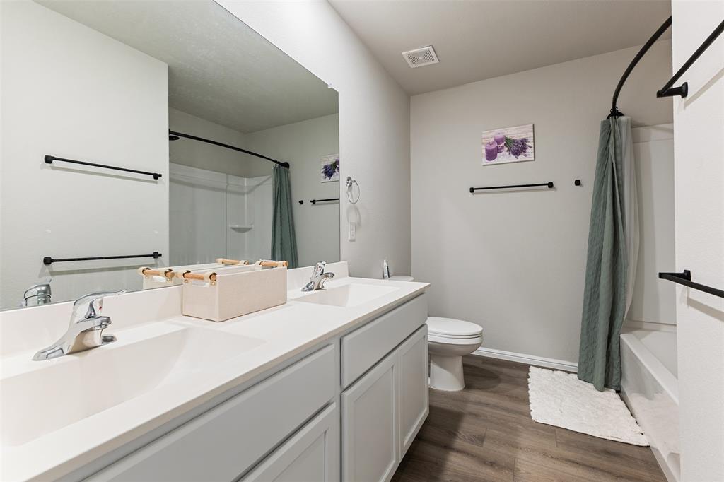Bathroom featuring dark wood-type flooring, double vanity, and shower / bath combination with curtain