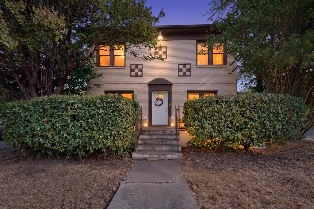 Brick exterior with decorative checkered accents, mature trees, and a concrete pathway leading to the entrance