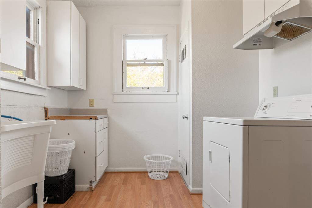 Wood-finish flooring with white walls, white cabinetry, and a utility sink
