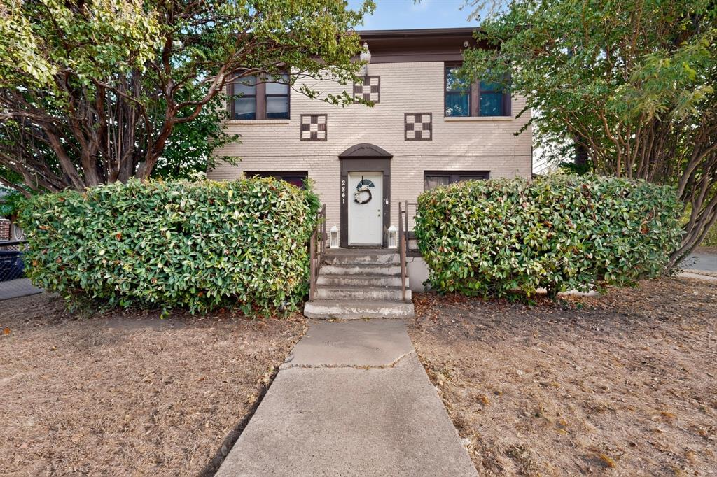 Brick exterior featuring decorative square accents, mature trees, and established perimeter hedging