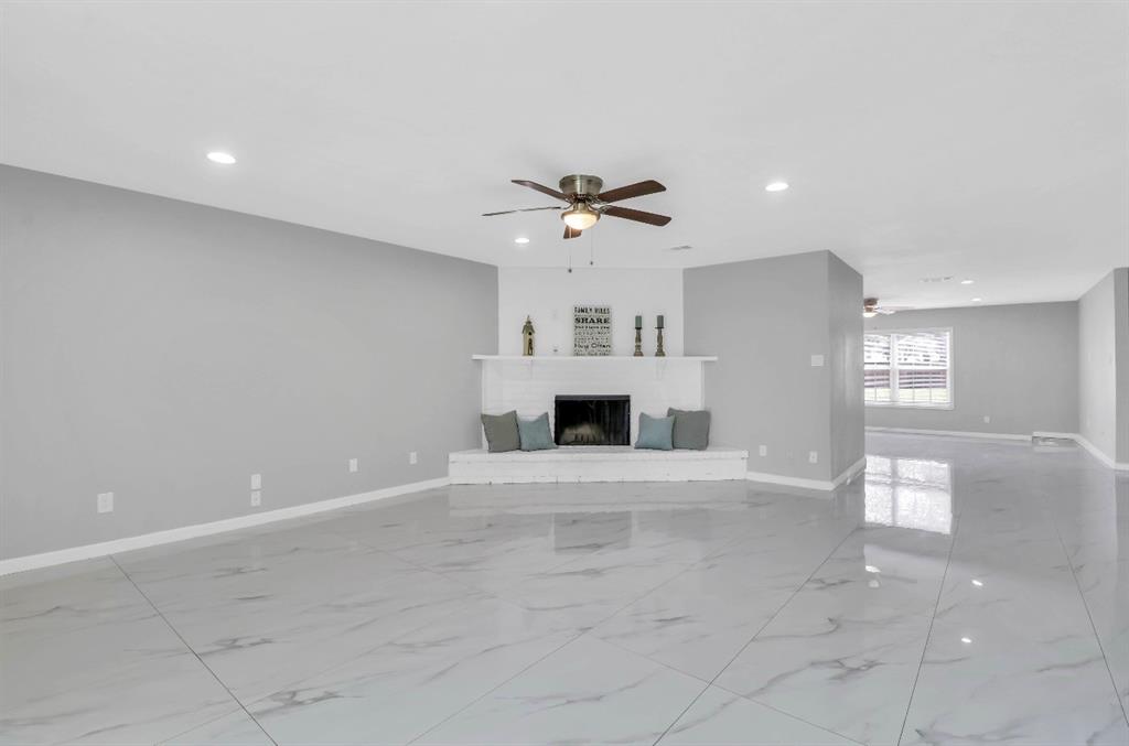 Spacious living area featuring a white brick fireplace with mantel, ceiling fan, recessed lighting, and large format tile flooring