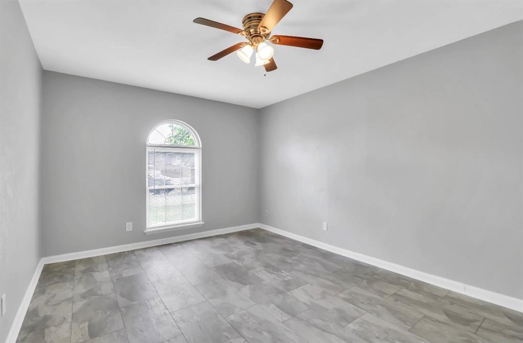 Spacious room featuring light gray walls, wood-finish flooring, and a ceiling fan with integrated lighting