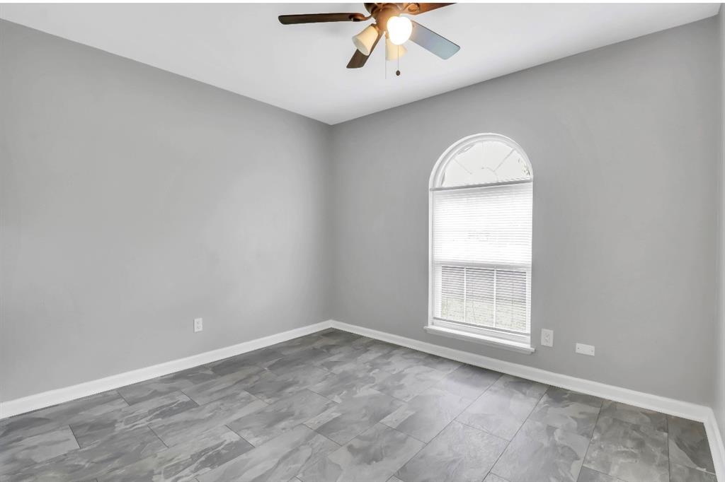 Room featuring a prominent arched window, grey wall paint, wood-finish flooring, white baseboards, and a ceiling fan with integrated lighting