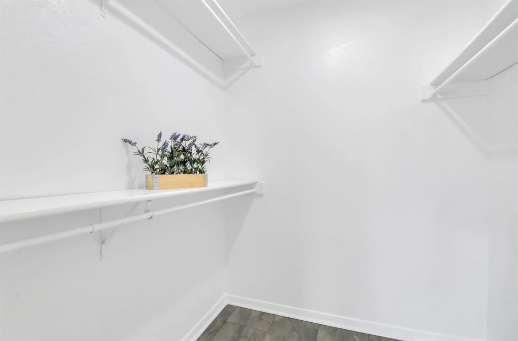 Spacious closet featuring white painted walls, white shelving, white hanging rods, and wood-finish flooring