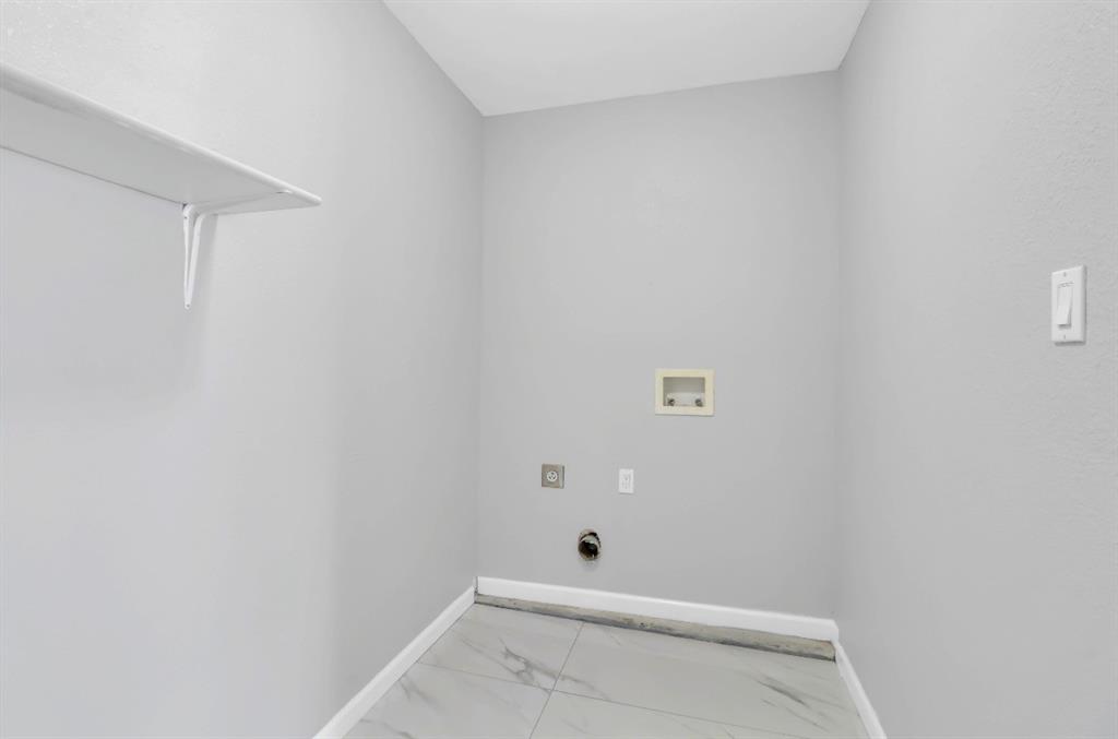 Dedicated utility space featuring light gray walls, a built-in white shelf, and light-toned tile flooring