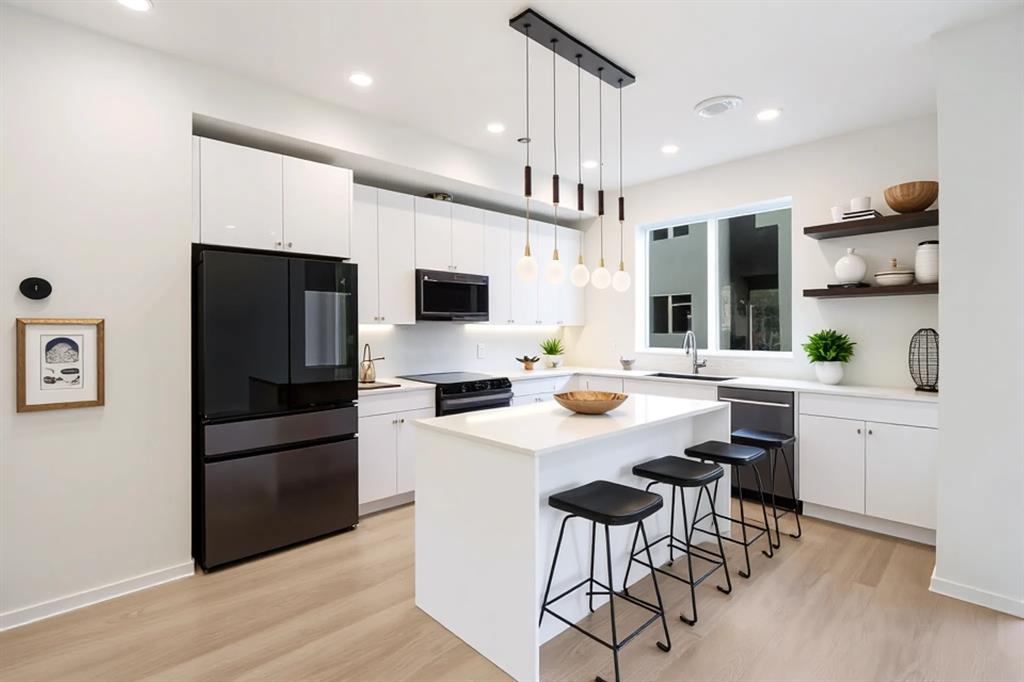Gourmet kitchen featuring a central island, pendant lighting, stainless steel appliances, white cabinetry, and wood-finish flooring