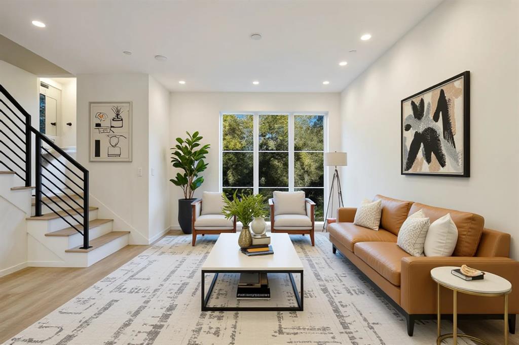 Recessed lighting illuminates the open-concept space, featuring wood-finish flooring and a staircase with contemporary black railings