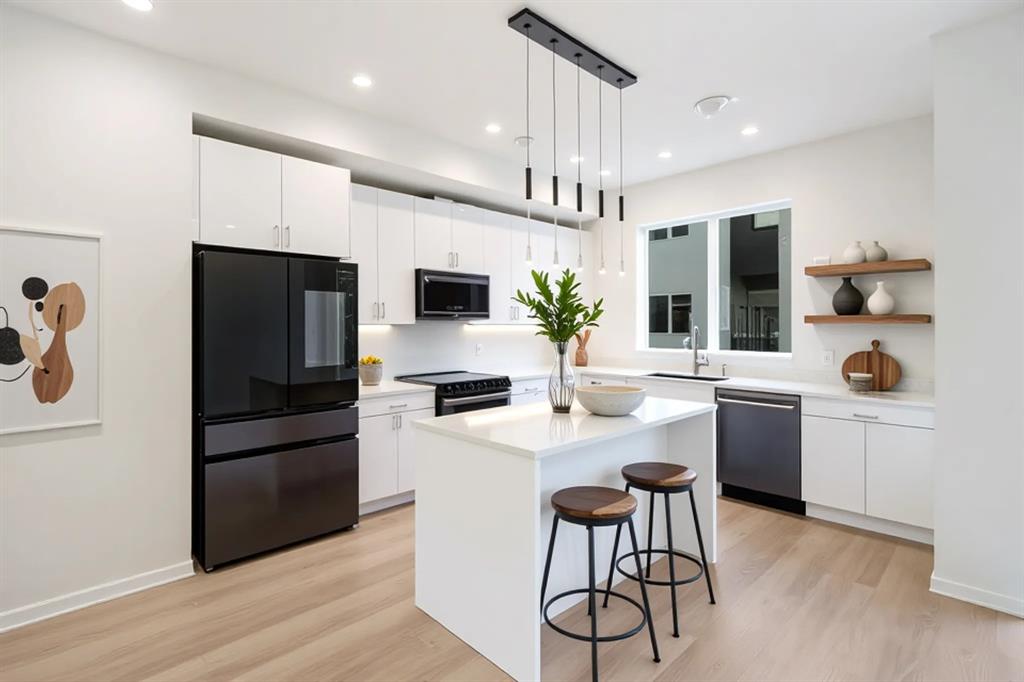 Contemporary kitchen featuring light wood-finish flooring, white cabinetry, dark-finish appliances, and a central island with pendant lighting