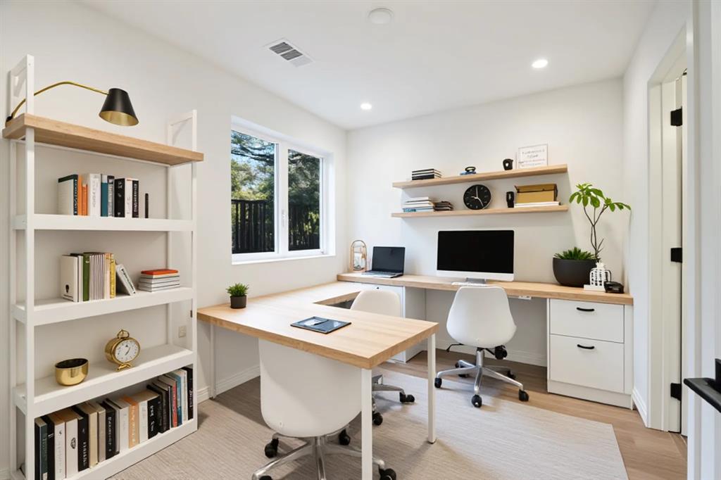 Integrated wood-finish desk with white cabinetry, built-in shelving, recessed lighting, and a large window