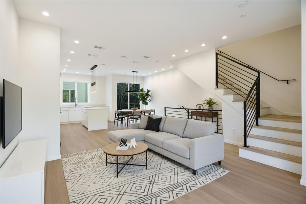 Open-concept living space featuring wood-finish flooring, recessed lighting, and a modern staircase with black metal railings