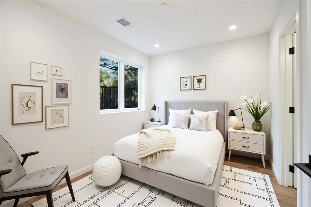 Recessed lighting illuminates the space, featuring a large window, wood-finish flooring, and crisp white walls