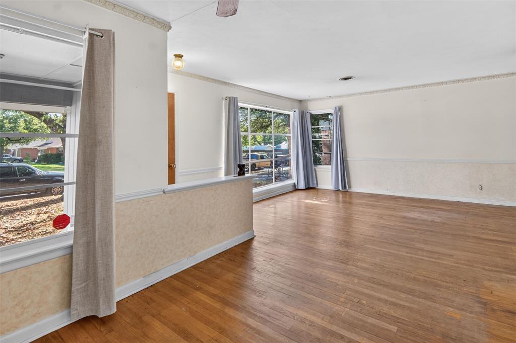 Hardwood flooring throughout, multiple large windows, cased openings, crown molding, and a partial wall with textured detailing Hardwood flooring throughout, multiple large windows, cased openings, crown molding, and a partial wall with textured detailing