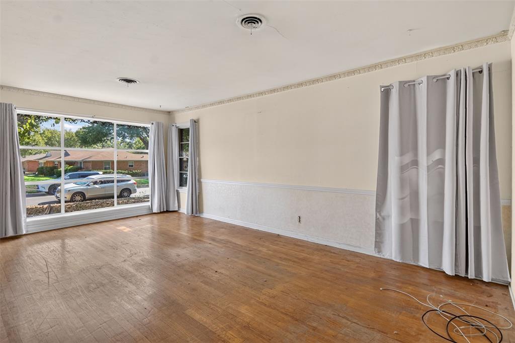 Expansive front window with multiple panes, wood-finish flooring, textured wainscoting, decorative ceiling trim, and multiple wall outlets Expansive front window with multiple panes, wood-finish flooring, textured wainscoting, decorative ceiling trim, and multiple wall outlets