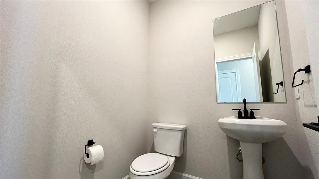 Pedestal sink with a matte black faucet, wall-mounted mirror, and white toilet