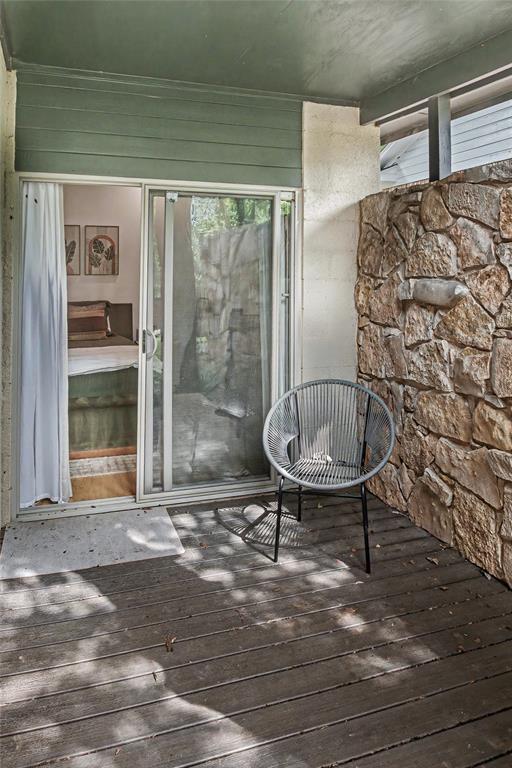 Covered patio off the primary suite featuring wood-finish decking and natural stone wall