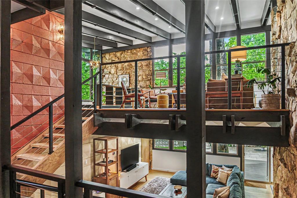 Multi-level interior featuring exposed steel beams, floor-to-ceiling natural stone wall, decorative geometric masonry, cable-railing staircase, and expansive window walls