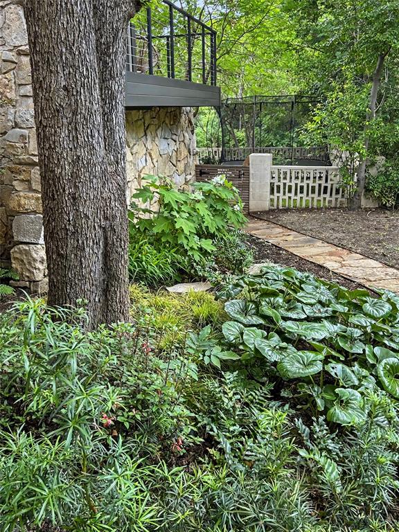 Natural stone exterior wall, elevated deck with dark metal railings, flagstone walkway, and mature native landscaping