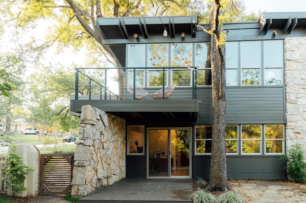 Mid-century modern exterior featuring natural stone masonry, treehouse balcony, expansive floor-to-ceiling windows, and a covered lower-level walkout patio.