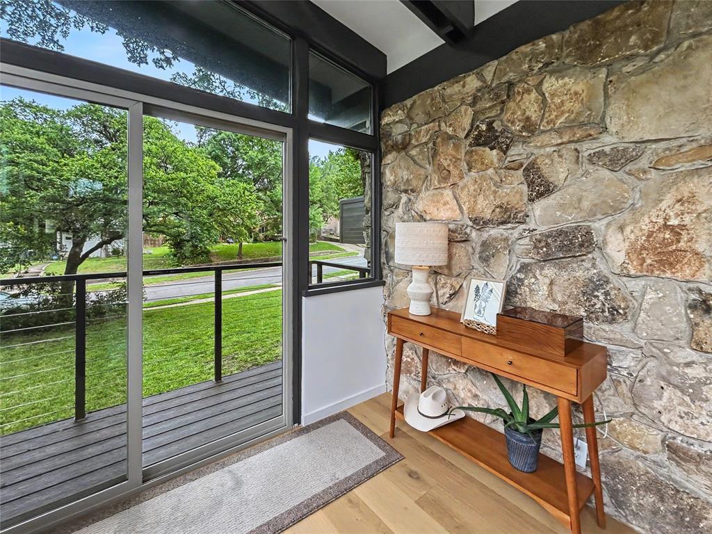 Stacked stone accent wall, hardwood flooring, and floor-to-ceiling wall of windows opening up to one of many balconies